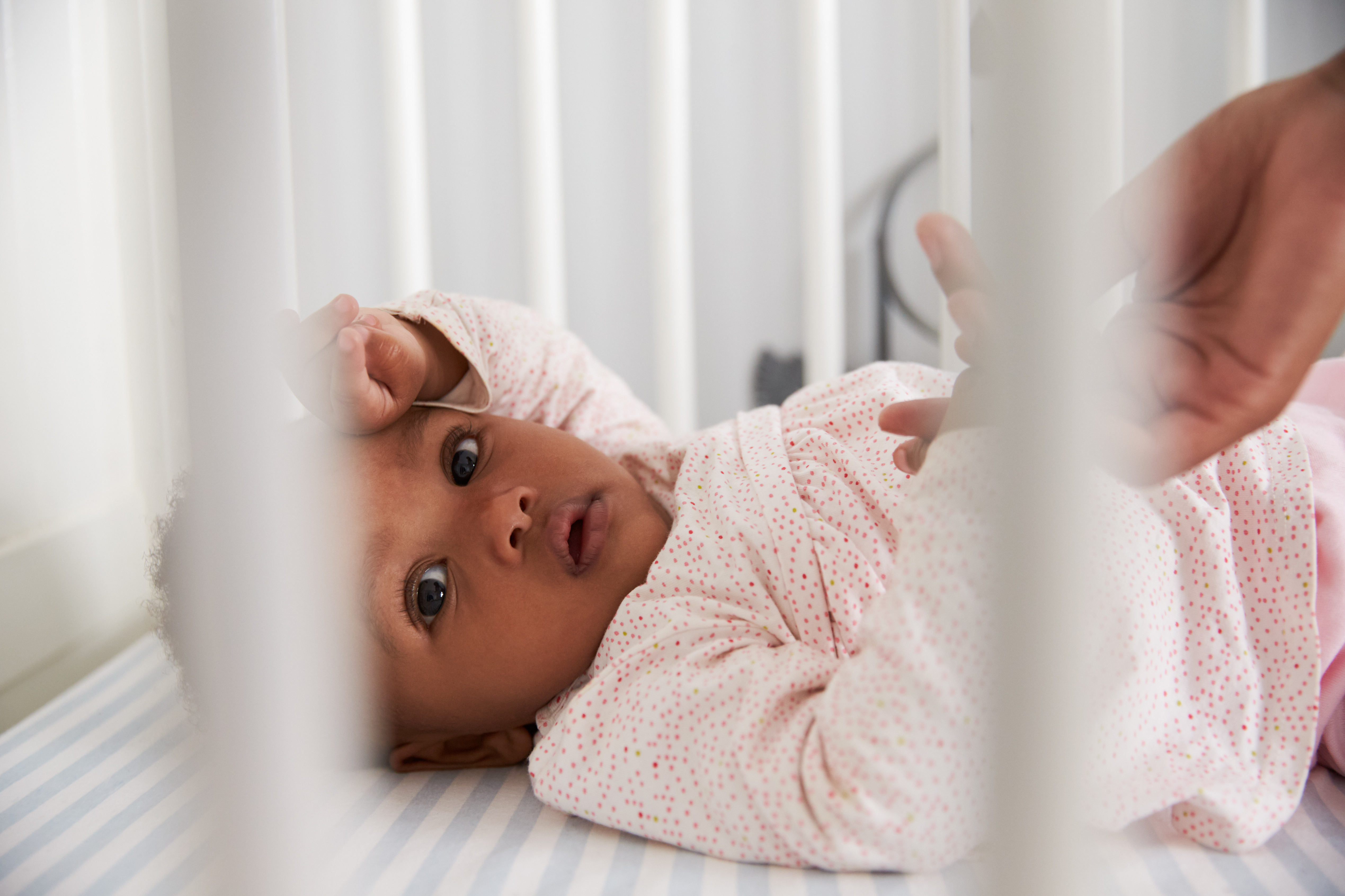 A baby wearing a pink outfit lays in a crib